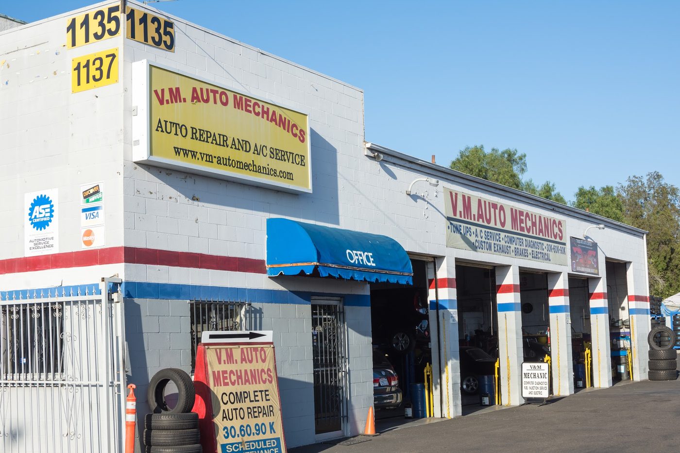 Yellow V.M. Auto Mechanics 'Auto Repair and A/C Service' sign over the office and service bays